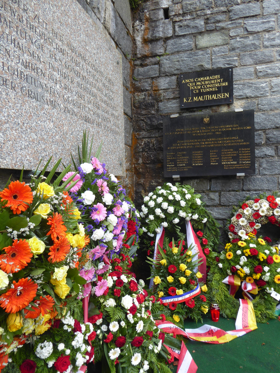 Plaque commémorative à l'entrée nord du tunnel de loibl et gerbes de fleurs au premier plan.